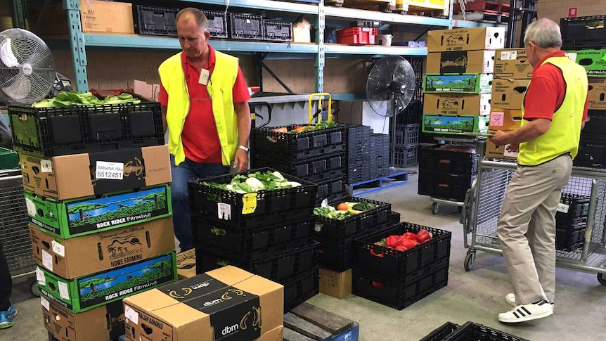 Food Rescue volunteers sort through boxes of produce, with racks of boxes behind them.