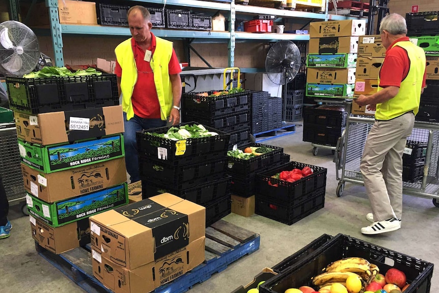 Food Rescue volunteers sort through boxes of produce, with racks of boxes behind them.