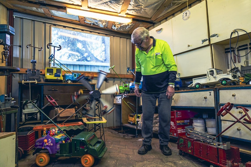 Oscar wears a high-vis top and stands in a workshop with a toy car behind him