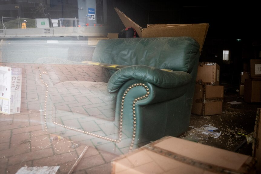 An armchair sits in an empty store window, surrounded by boxes and clutter.