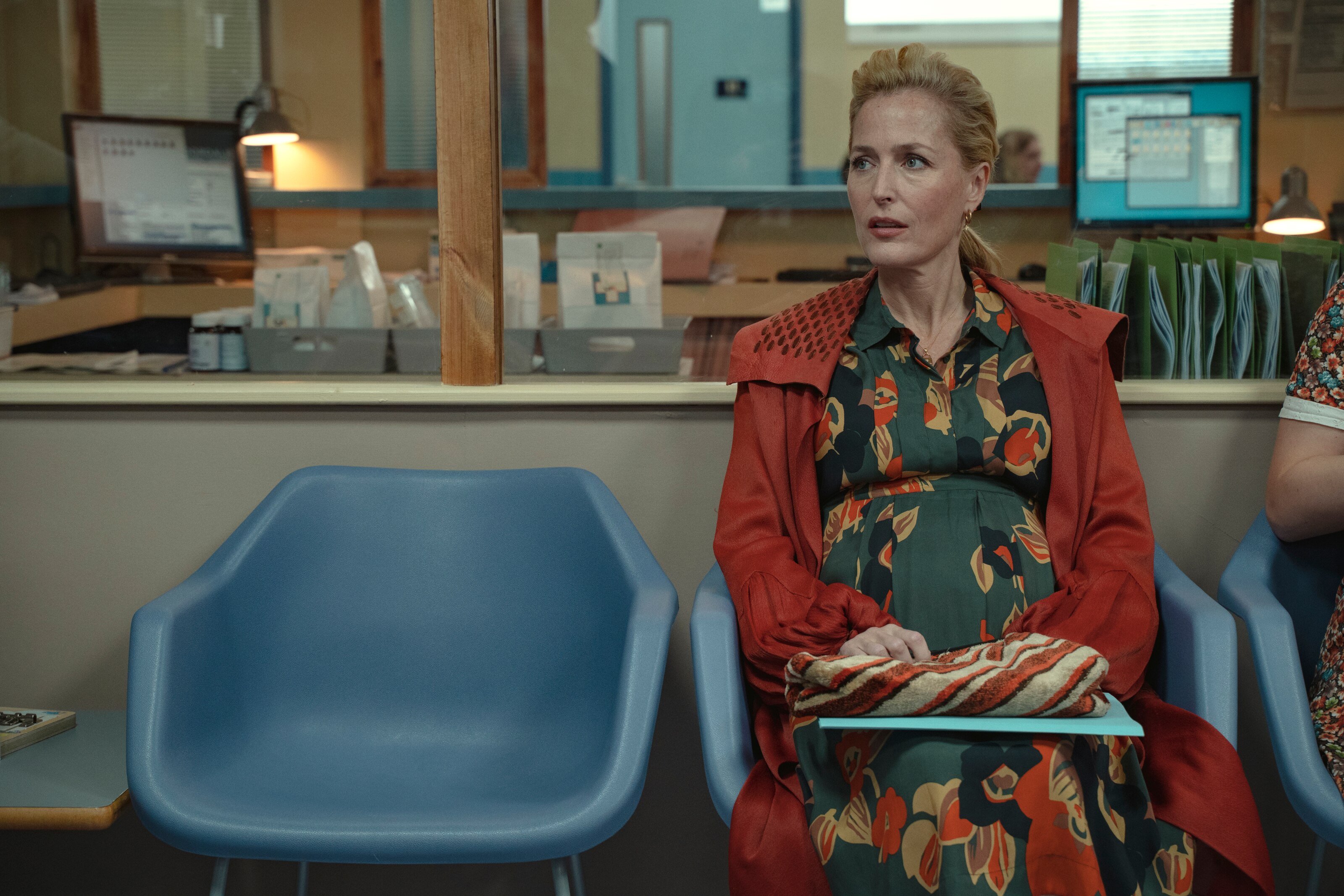 Jean Milburn (Gillian Anderson) from Sex Education sits in a doctor's waiting room, heavily pregnant.