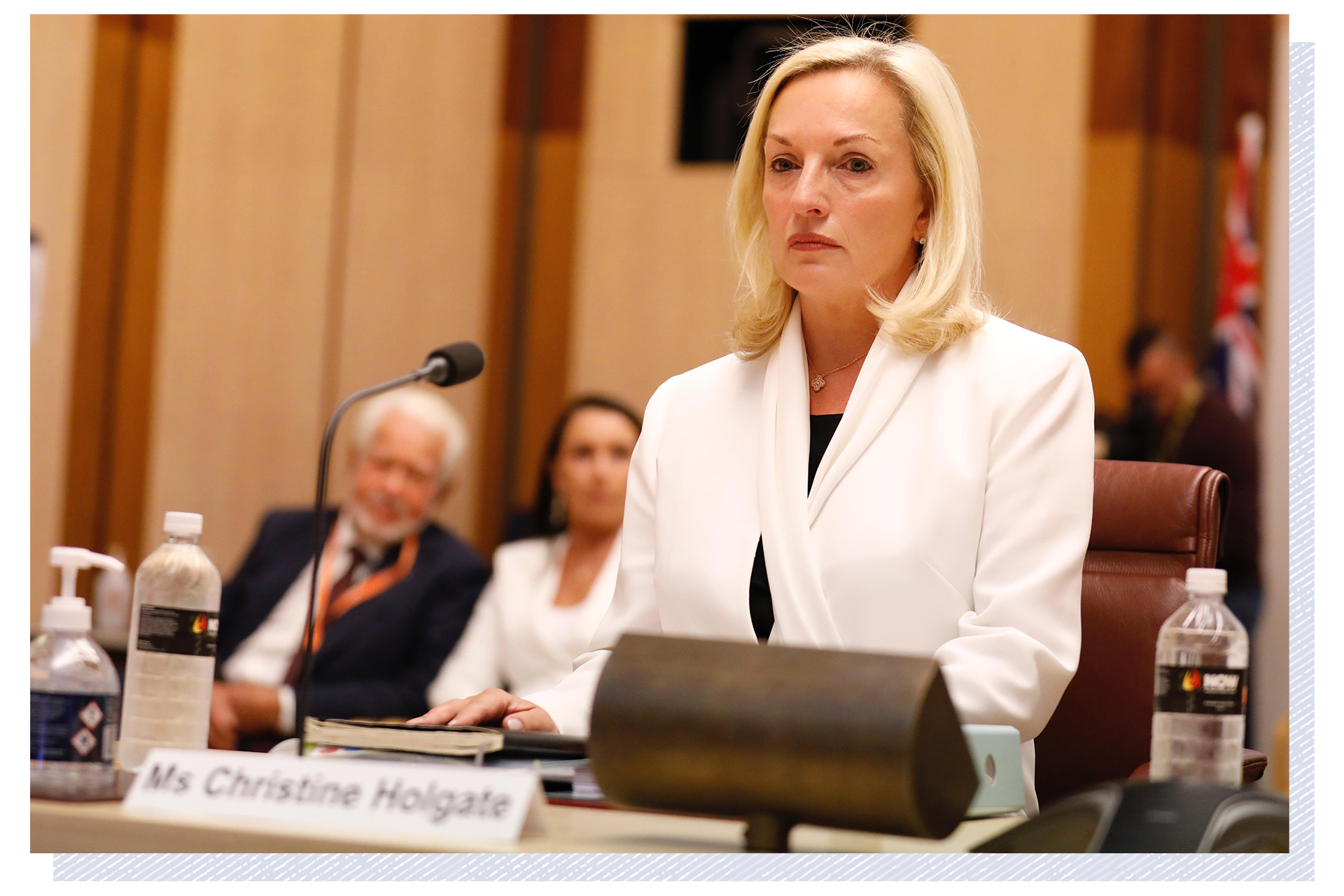 Christine Holgate wears a white jacket and sits at a table, in front of a microphone, while giving evidence at a senate hearing.