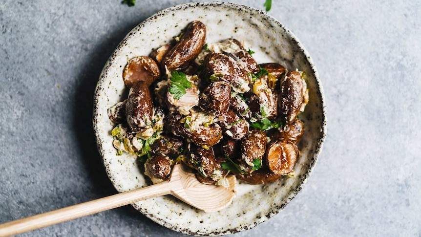 A bowl of vegan potato salad with roasted kipfler potatoes, dressing, parsley and caramelised leeks for a festive recipe.