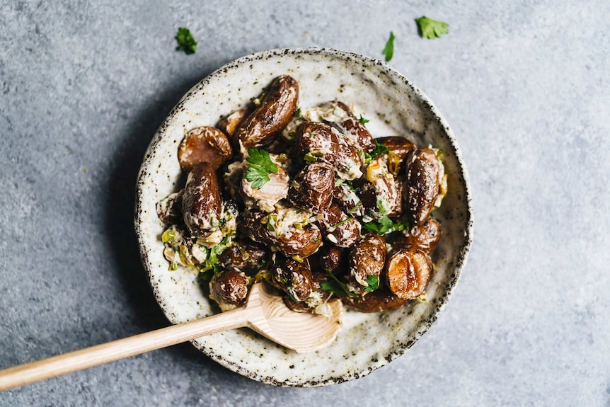 A bowl of vegan potato salad with roasted kipfler potatoes, dressing, parsley and caramelised leeks for a festive recipe.