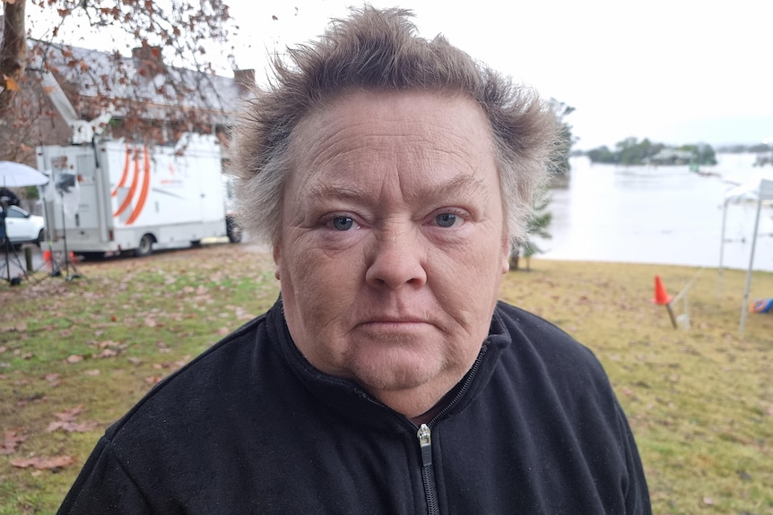 A woman stands next to a flooded river