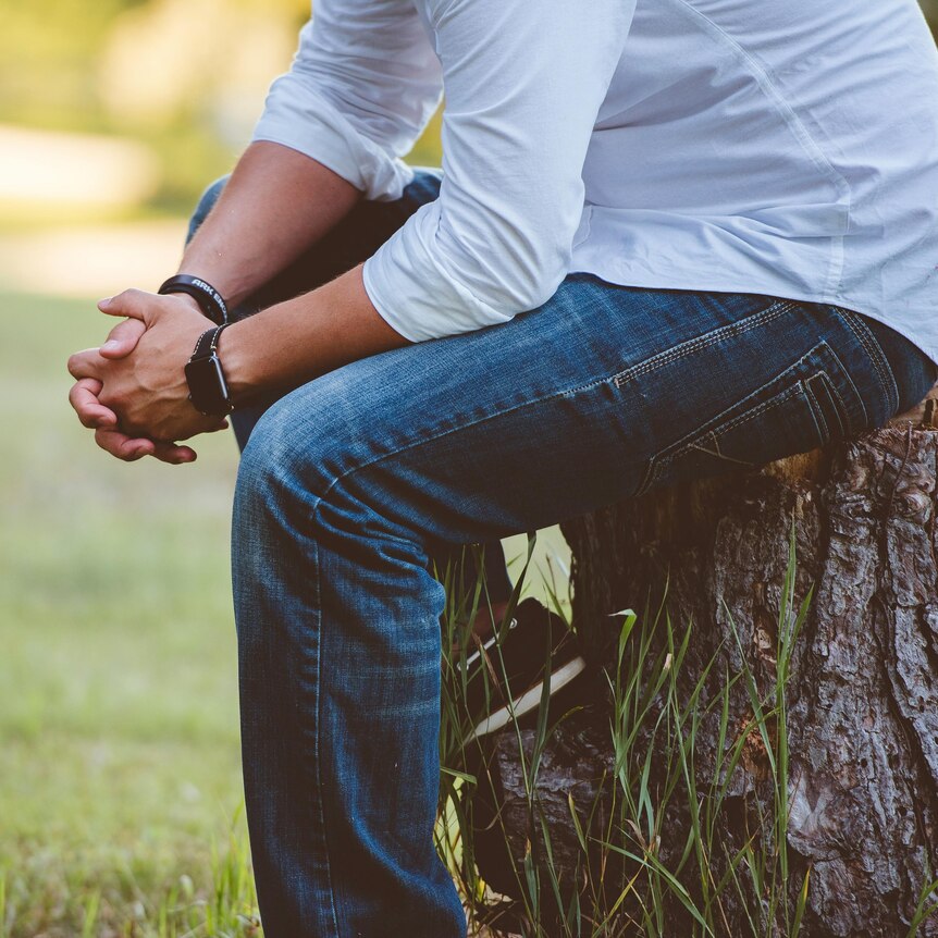A man looking despairing, sitting on a log in a grassy paddock.