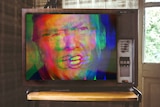 Trump's face in rainbow colours on a TV screen.