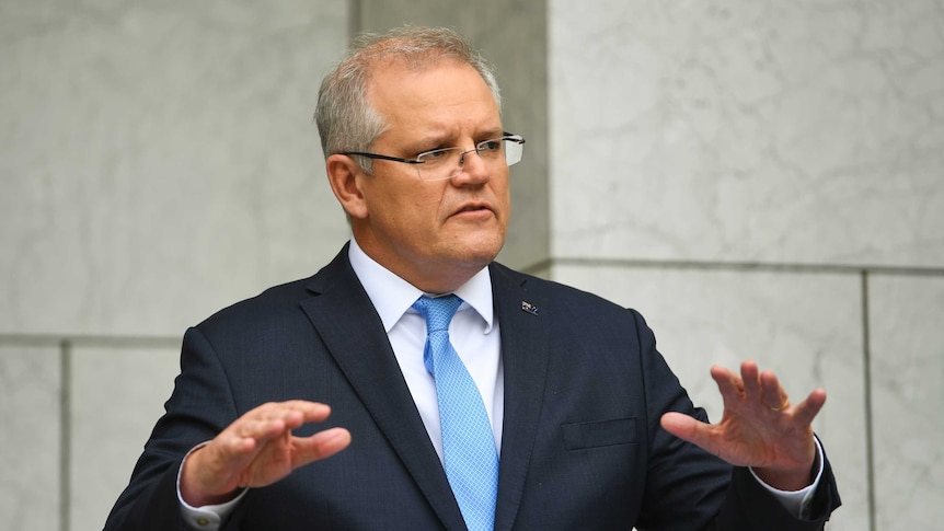 Australian Prime Minister Scott Morrison raises his hands while speaking at a press conference wearing a suit and blue tie