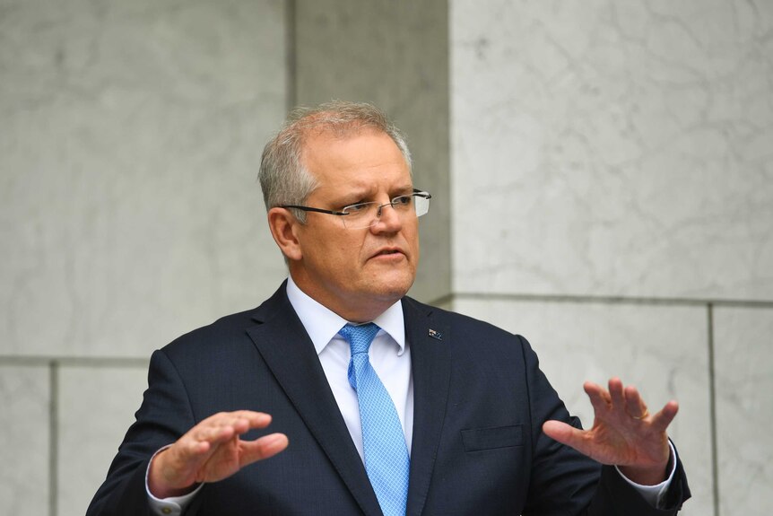 Australian Prime Minister Scott Morrison raises his hands while speaking at a press conference wearing a suit and blue tie