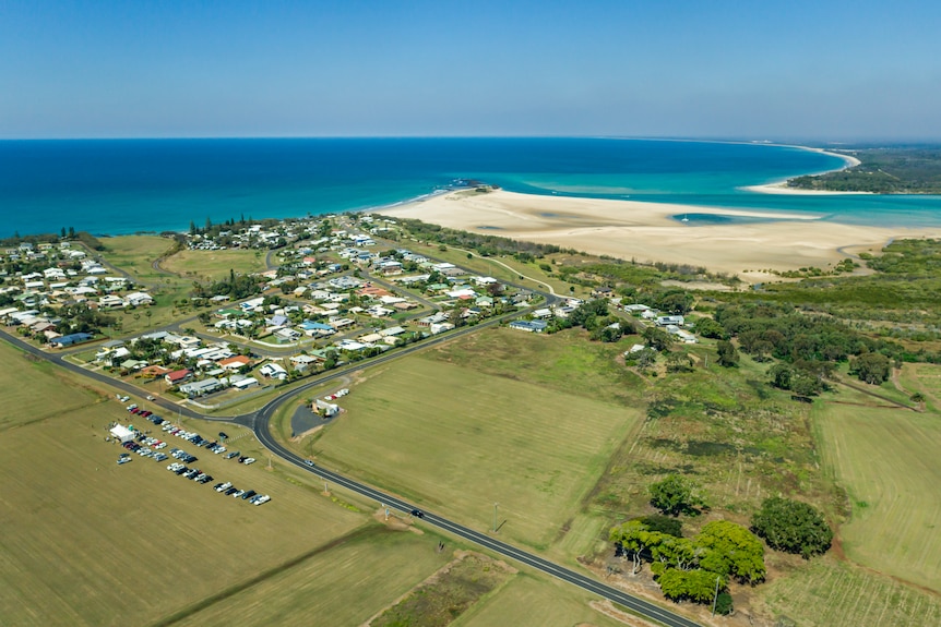 An aerial view of small beach town surrounded by paddocks.