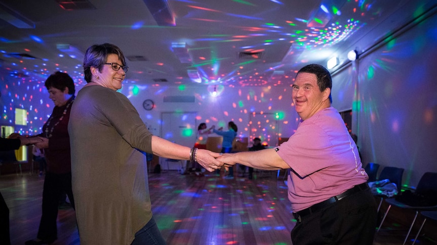 The pair hold hands and smile while dancing.