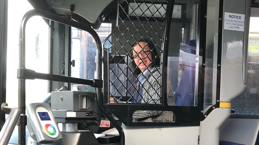 A woman sits in the drivers seat of a bus.