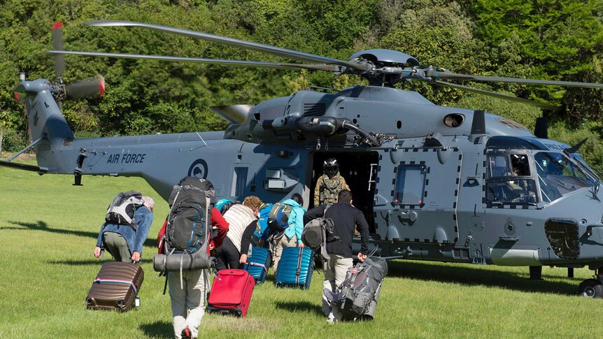 People run towards a helicopter with luggage