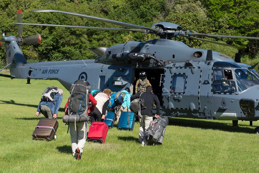 People run towards a helicopter with luggage