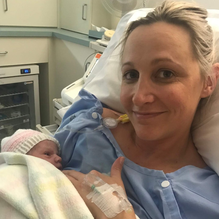 Woman sits in hospital bed smiling and holding a swaddled newborn