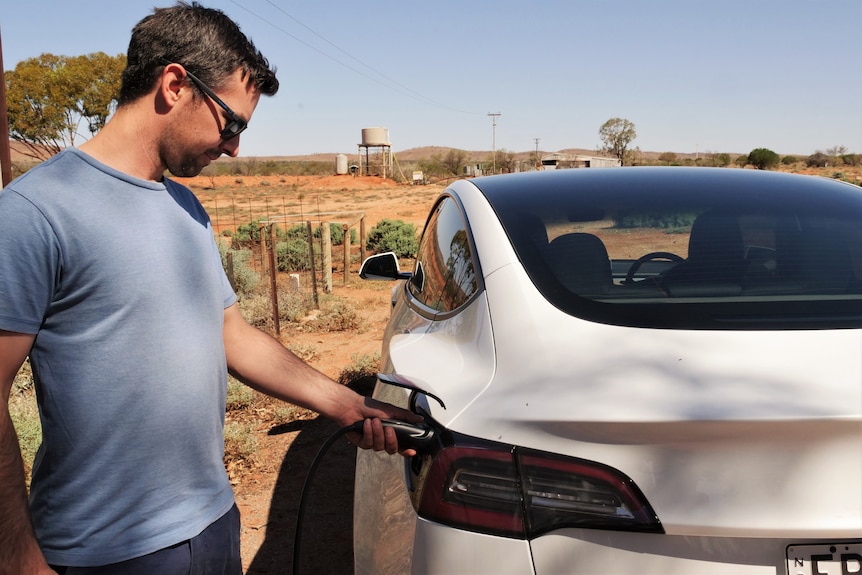 A man charging an electric vehicle on an outback station.