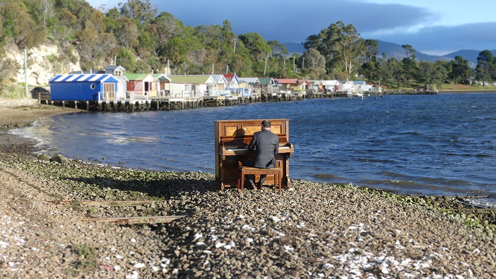 Tasmanian Kelvin Smith playing the piano next to water at Cornelian Bay.