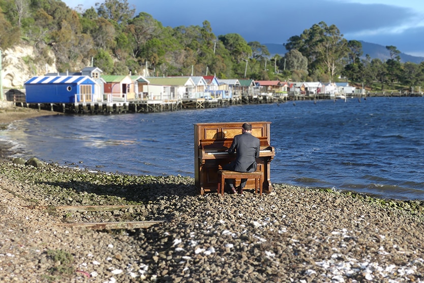 Tasmanian Kelvin Smith playing the piano next to water at Cornelian Bay.