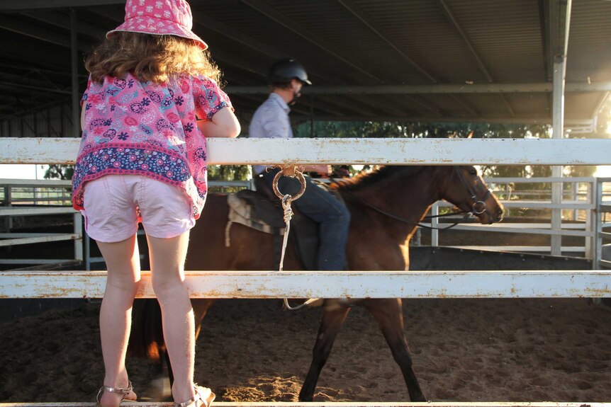 Six-year-old Bronte Brown watches as her new horse Coco is ridden by one of the Longreach Pastoral College students.