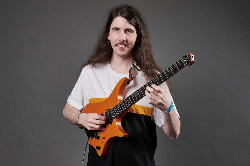 A man with dark long dark hair holding a guitar.