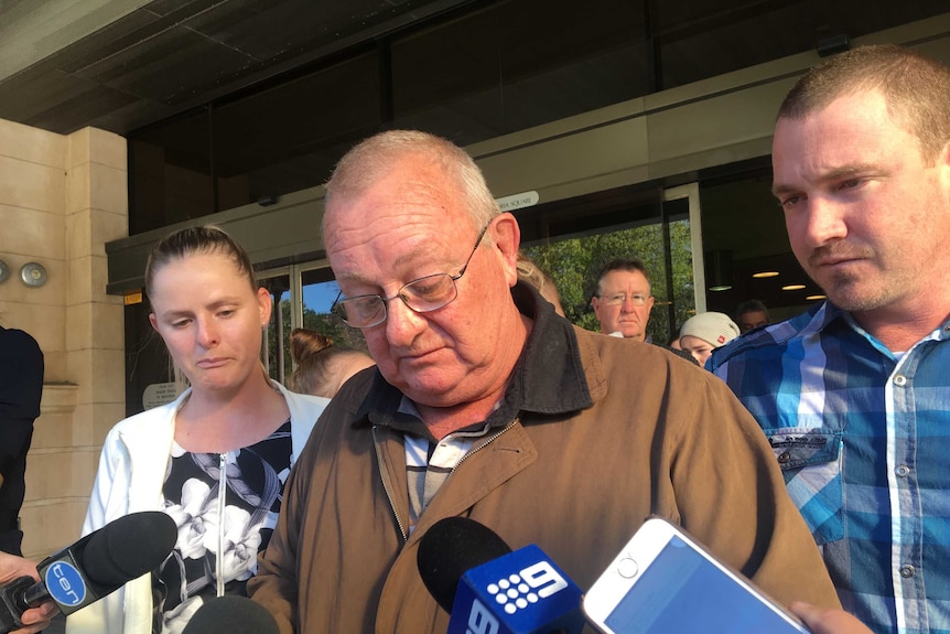 An emotional older man speaks to journalists outside a courtroom with his daughter and son by his side