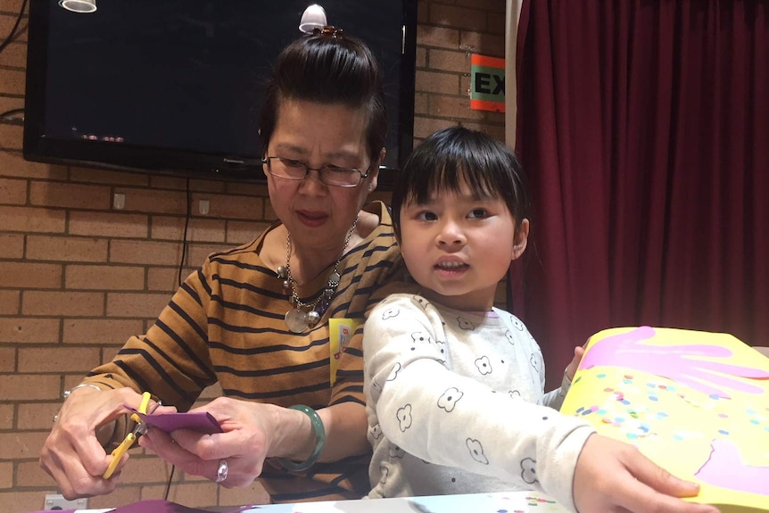 A presschool aged girl and an older woman make art from cardboard at a table.