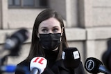 A young female politician wears a black face mask as she speaks into the mics of assembled media.