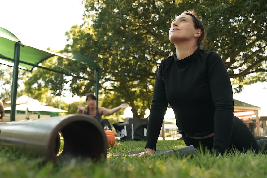 A woman holds a yoga pose in a park.