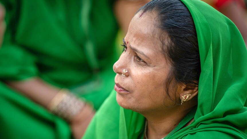 A woman in a bright green sari looking thoughtful