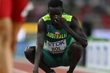 Peter Bol crouches down and puts his hand on his face, looking disappointed after a race
