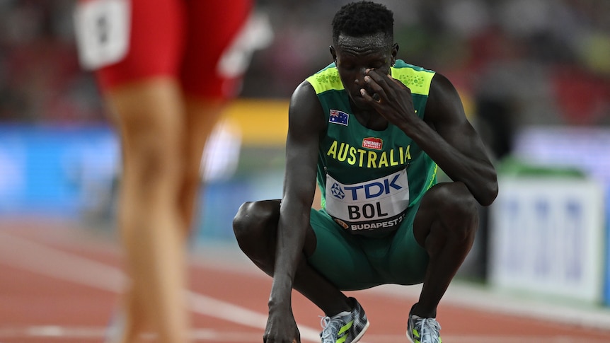 Peter Bol crouches down and puts his hand on his face, looking disappointed after a race