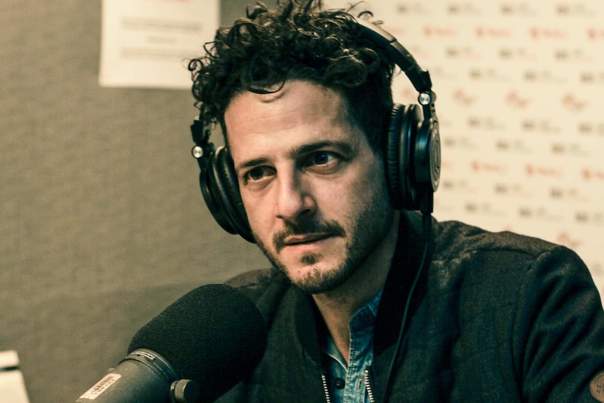 Lior at a microphone with headphones on as he's interviewed for the radio