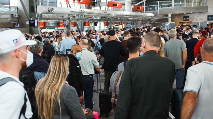 People wearing masks and carrying bags line up in long queues