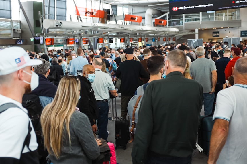 People wearing masks and carrying bags line up in long queues