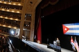 Barack Obama stands on stage to deliver a speech in a big theatre.