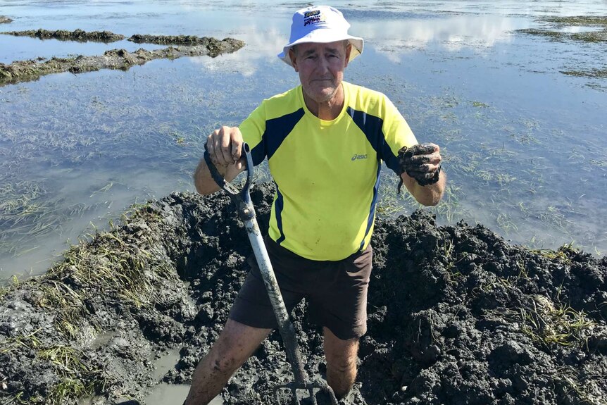 Martin Cowling with his pitchfork in one hand and a bloodworm in the other and seagrass beds behind him.