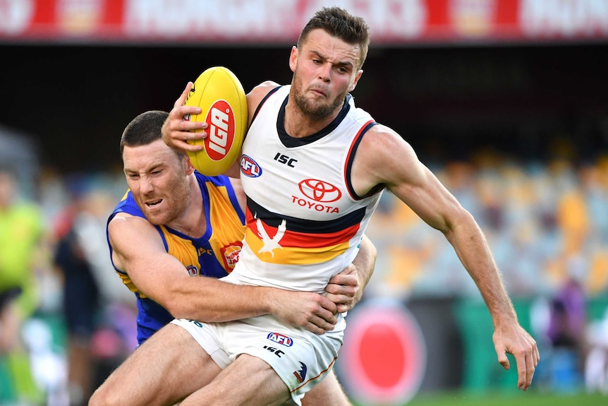 An Adelaide Crows AFL players holds the ball while he is tackled by a West Coast Eagles opponent.