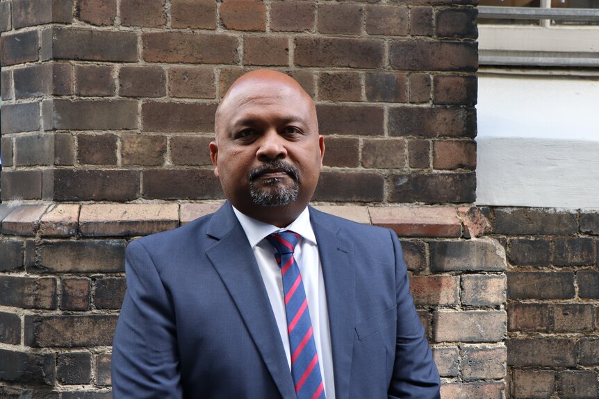NSW Teacher Federation Acting President Henry Rajendra stands in front of a brick wall