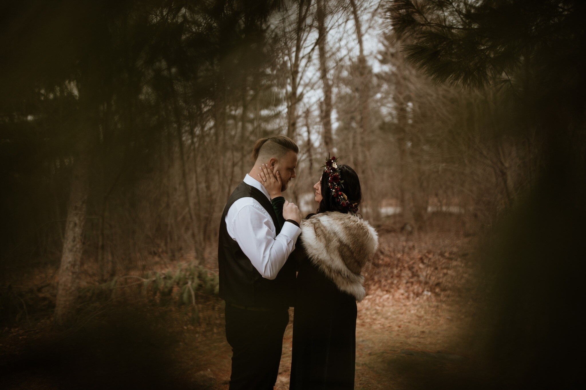 A man and woman stand in the woods looking at each other