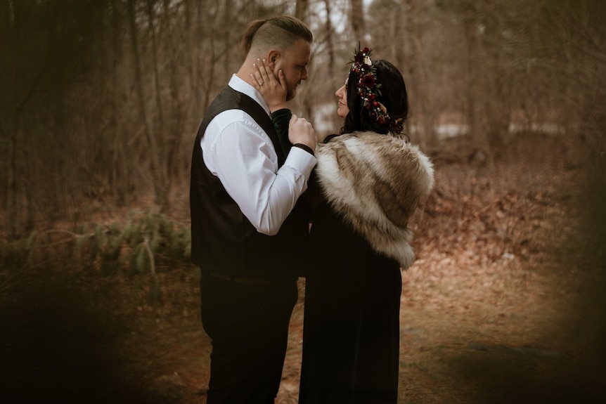 A man and woman stand in the woods looking at each other