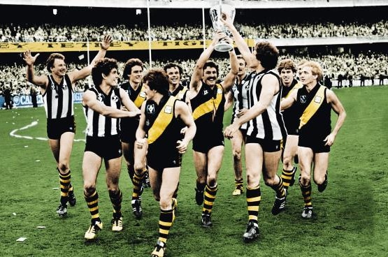 The victorious 1980 Richmond premiership side walk off the field holding the cup.