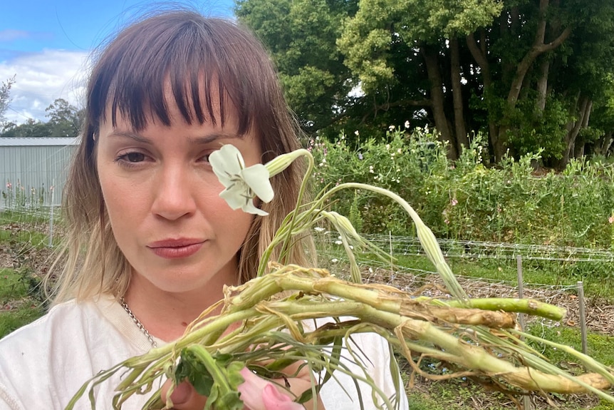 A woman looking unhappy and holding up an uprooted flower