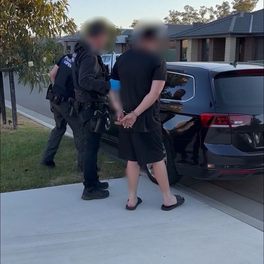 a man in a black t-shirt and black pants is placed in a police car