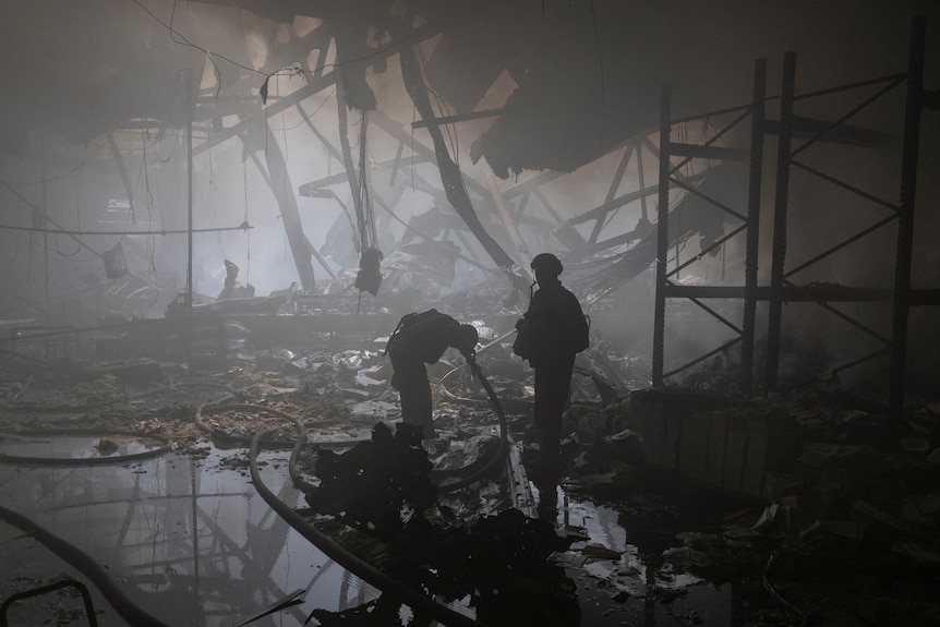 two firefighters stand in the middle of the ruins of a factory 