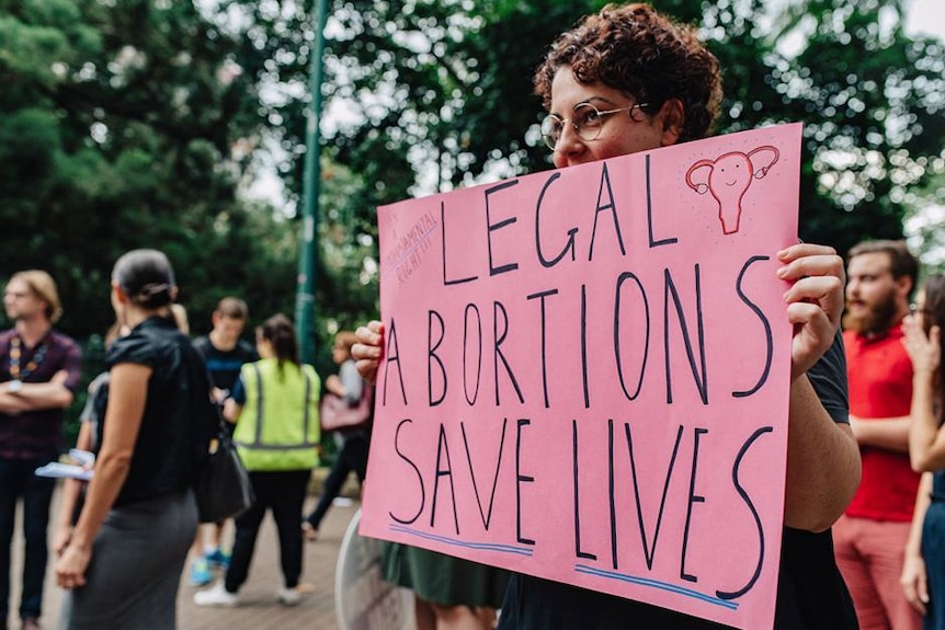 A woman holds a sign at a pro-choice rally, saying legal abortions save lives