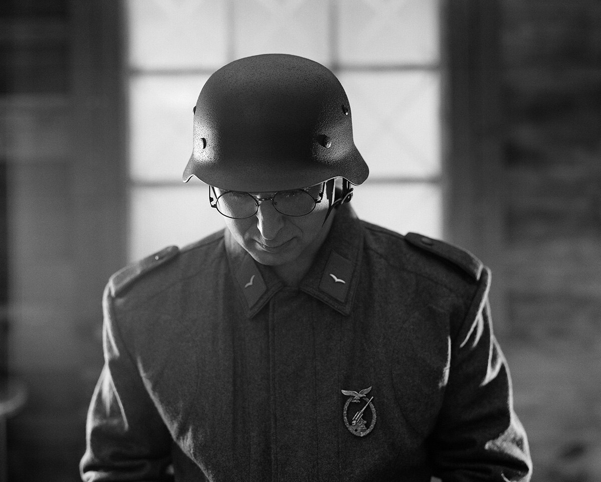 Black and white photographic artwork of a soldier looking down and standing in uniform and hard helmet in dimly lit interior.