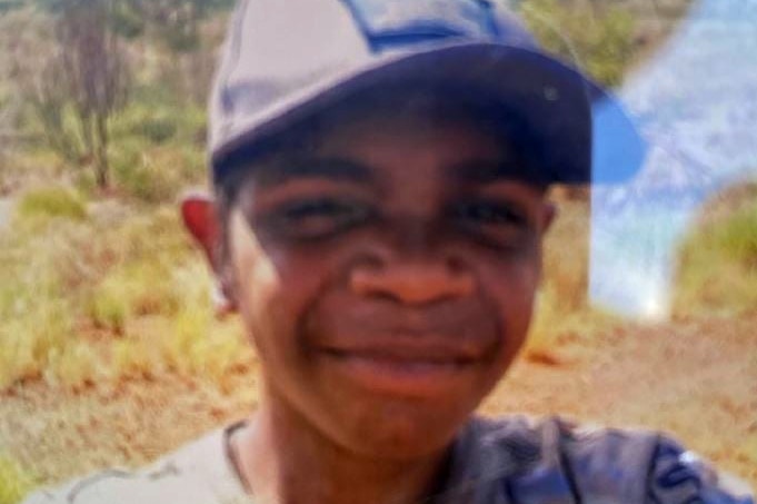 A boy with a hat on, smiling at the camera