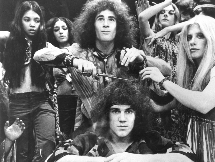 A black and white photo of the 1968 Broadway cast of Hair cutting off a character's hair