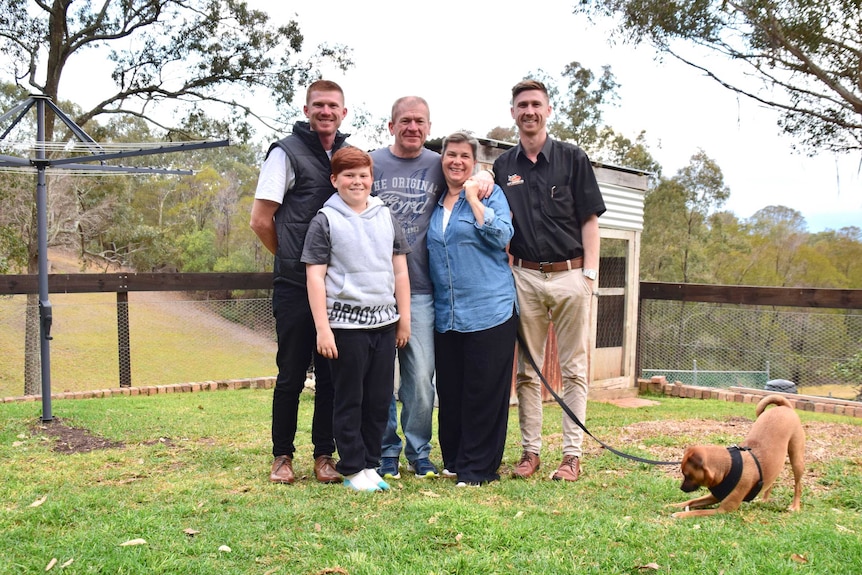 The James family stand in their backyard next to a clothes line and shed, supporting Pete James who has younger onset dementia.