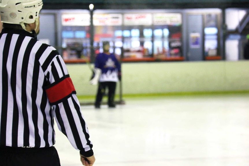 Referee watching over a broomball match on an ice rink.